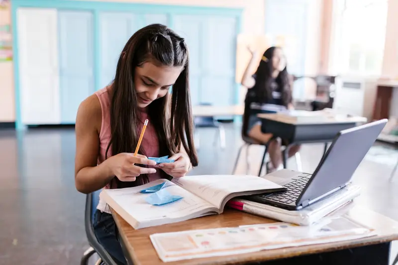 Una estudiante de colegio trabaja en su escritorio con un libro y una computadora