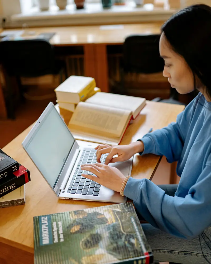 Una joven estudia con libros y su computadora portátil en una biblioteca