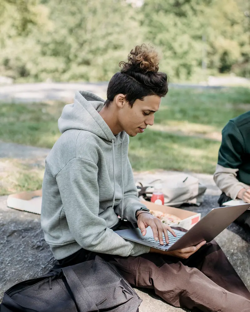 Un joven estudia con su computadora portátil sentado al aire libre